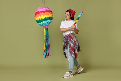 Photo of Happy woman hitting colorful pinata with stick on green background