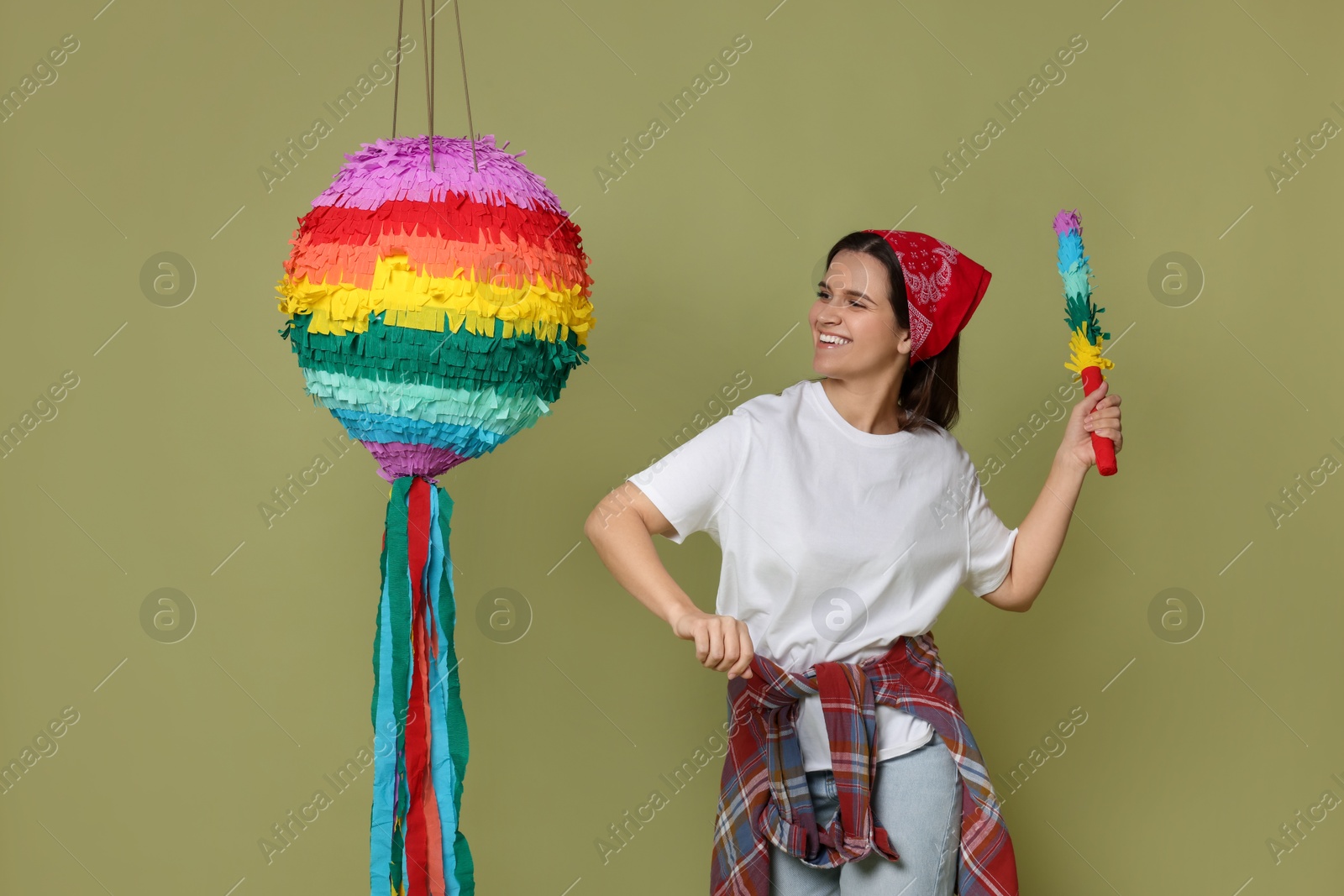 Photo of Happy woman hitting colorful pinata with stick on green background