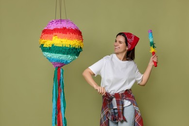 Photo of Happy woman hitting colorful pinata with stick on green background