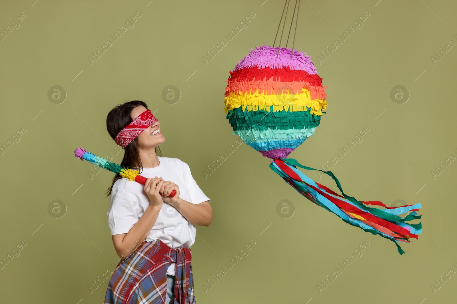 Photo of Woman with tied eyes breaking pinata on green background