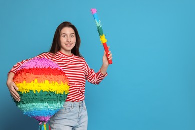 Photo of Happy woman with colorful pinata and stick on light blue background, space for text