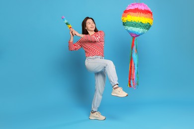 Photo of Happy woman hitting colorful pinata with stick on light blue background