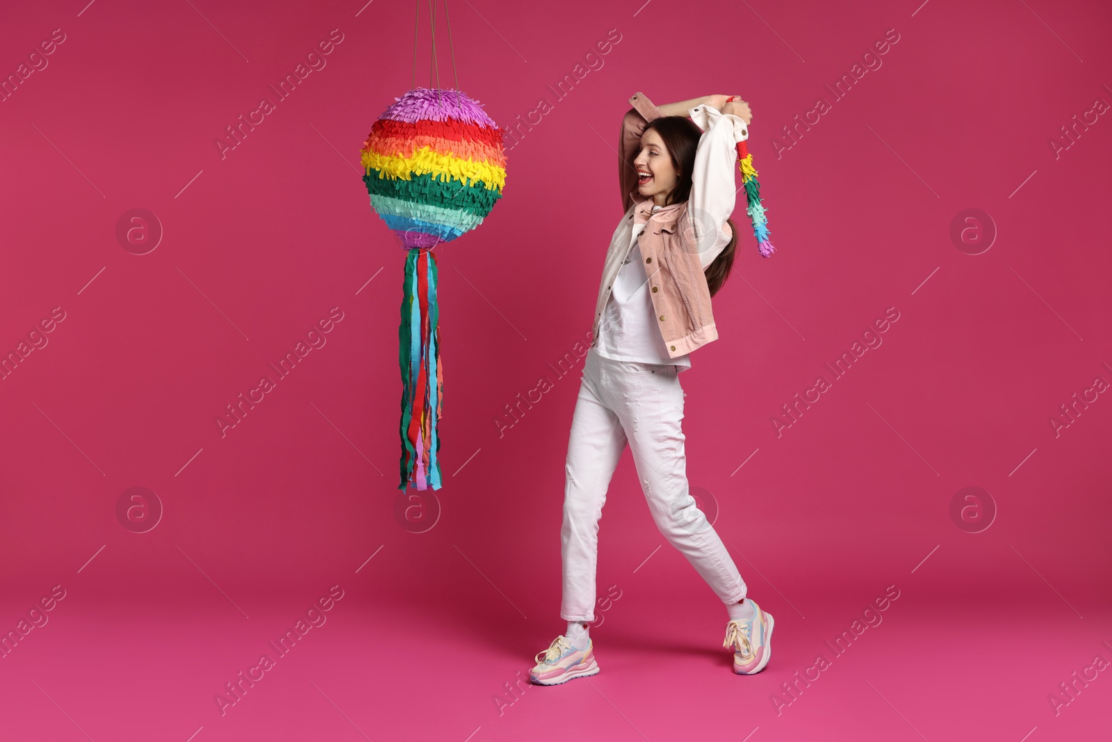 Photo of Happy woman breaking colorful pinata with stick on pink background