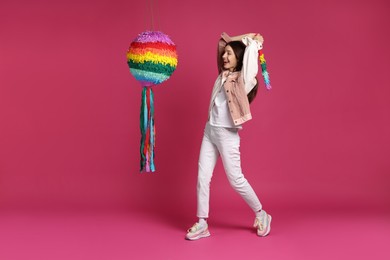 Photo of Happy woman breaking colorful pinata with stick on pink background