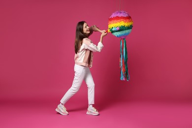 Photo of Happy woman breaking colorful pinata with stick on pink background