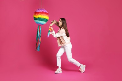 Photo of Happy woman breaking colorful pinata with stick on pink background