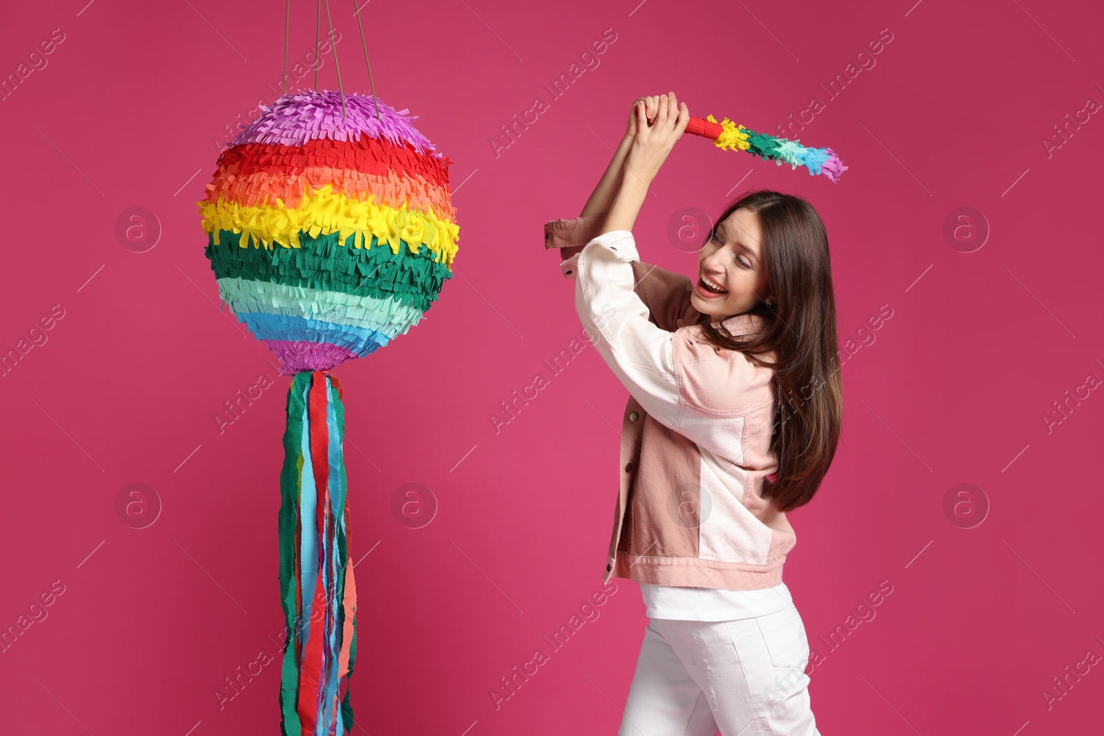 Photo of Happy woman breaking colorful pinata with stick on pink background