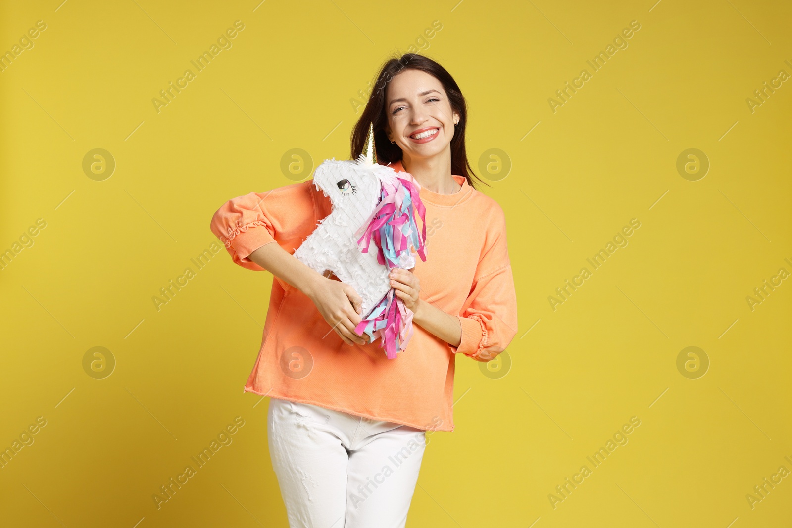 Photo of Happy woman with unicorn shaped pinata on yellow background