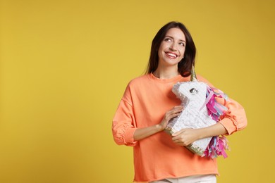 Photo of Happy woman with unicorn shaped pinata on yellow background, space for text