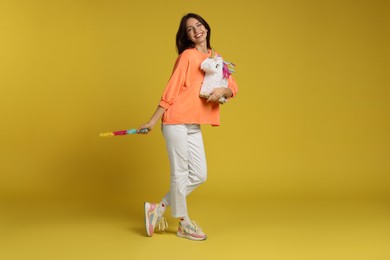 Photo of Happy woman with unicorn shaped pinata and stick on yellow background