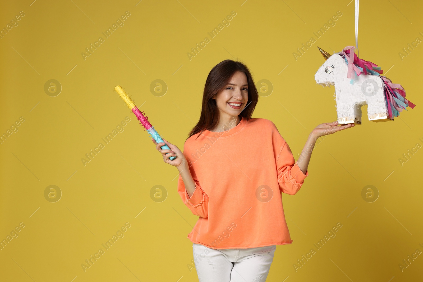 Photo of Happy woman with unicorn shaped pinata and stick on yellow background