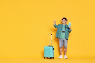 Photo of Traveller with passport and suitcase pointing at something on yellow background. Space for text