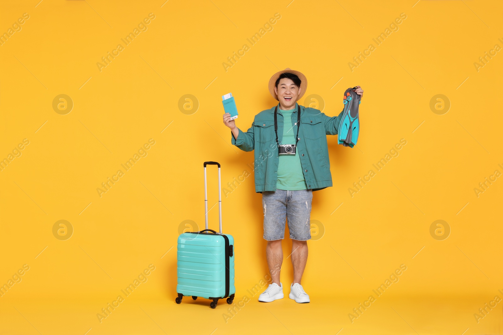 Photo of Traveller with passport, swim fins and suitcase on yellow background