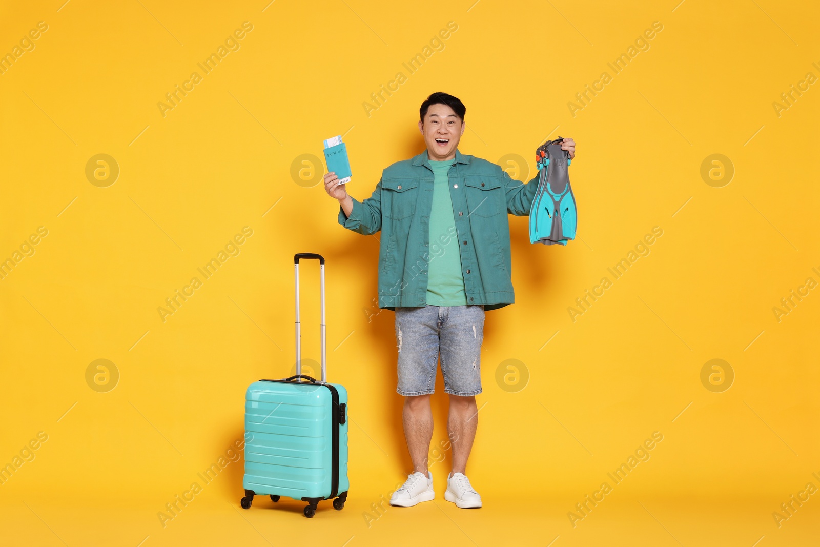 Photo of Traveller with passport, swim fins and suitcase on yellow background