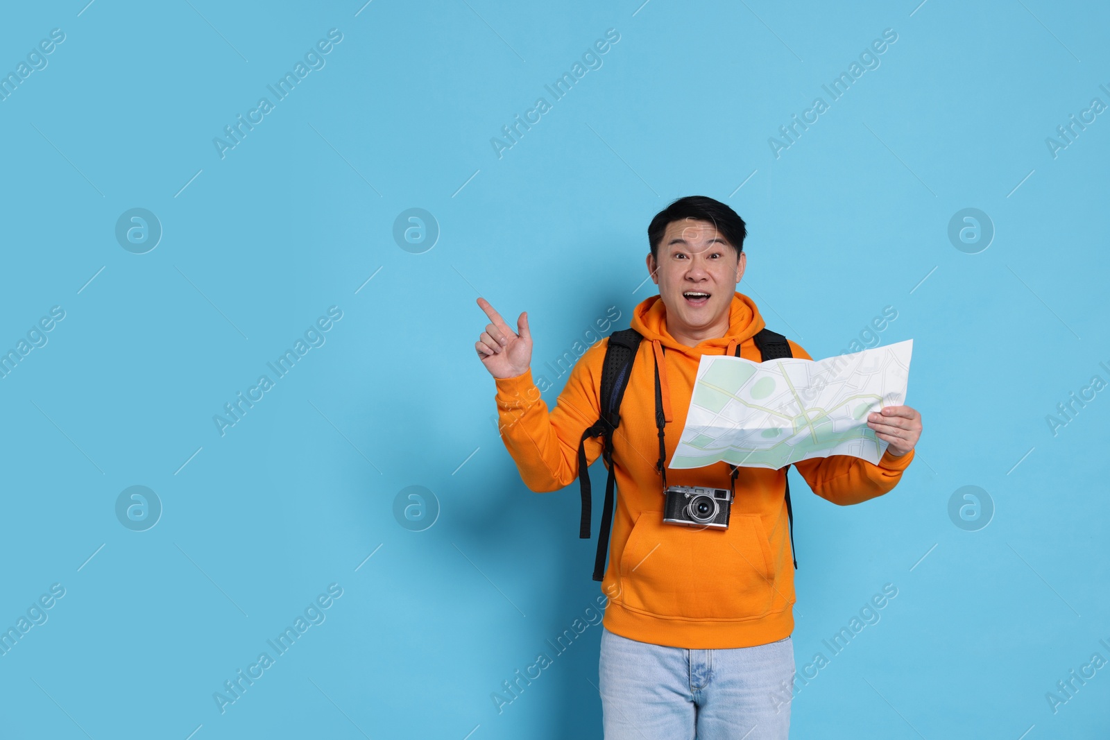 Photo of Happy traveller with map pointing at something on light blue background. Space for text