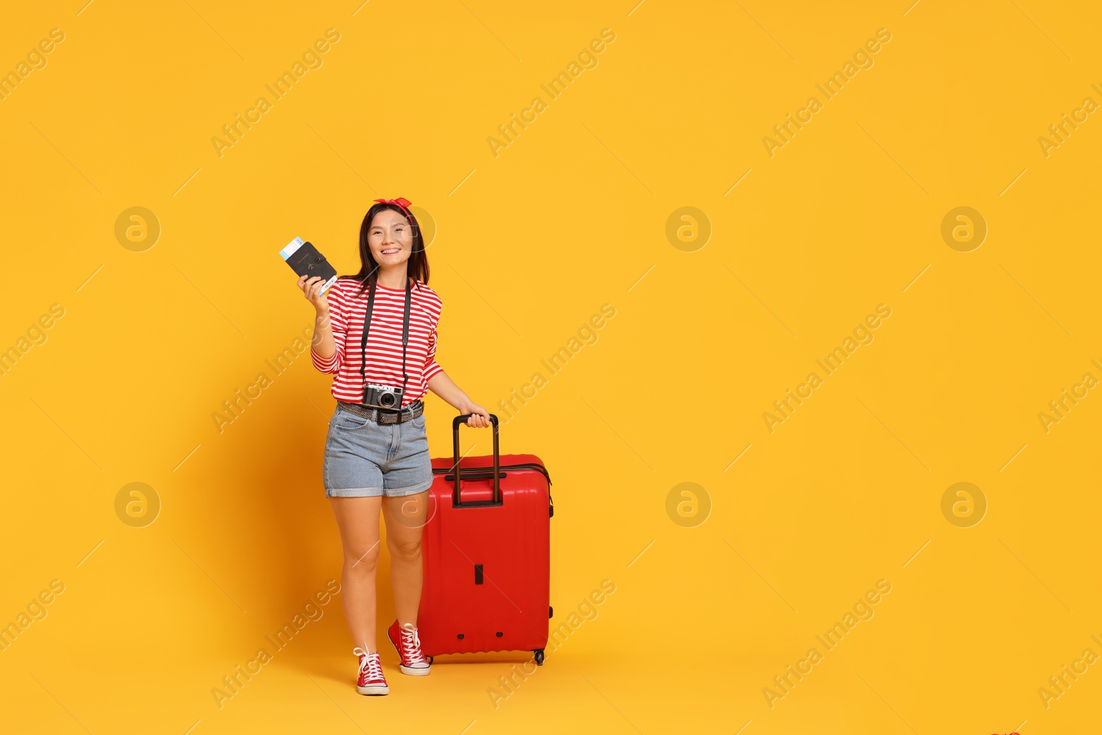 Photo of Happy traveller with passport and suitcase on yellow background