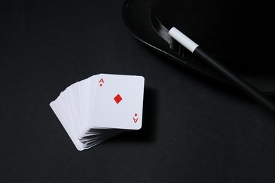 Photo of Playing cards, hat and magic wand on black background, closeup