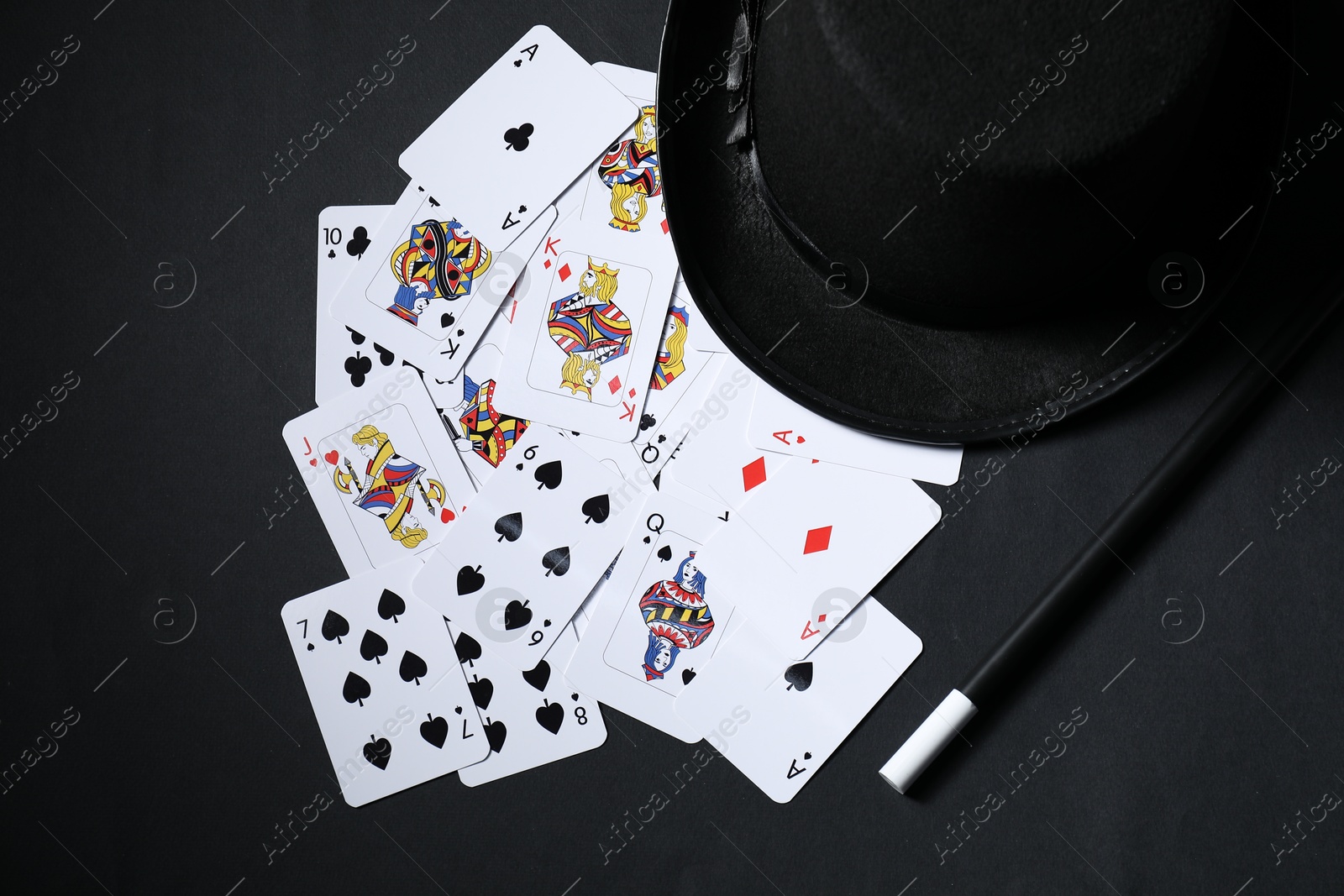 Photo of Playing cards, hat and magic wand on black background, top view