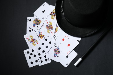 Photo of Playing cards, hat and magic wand on black background, top view