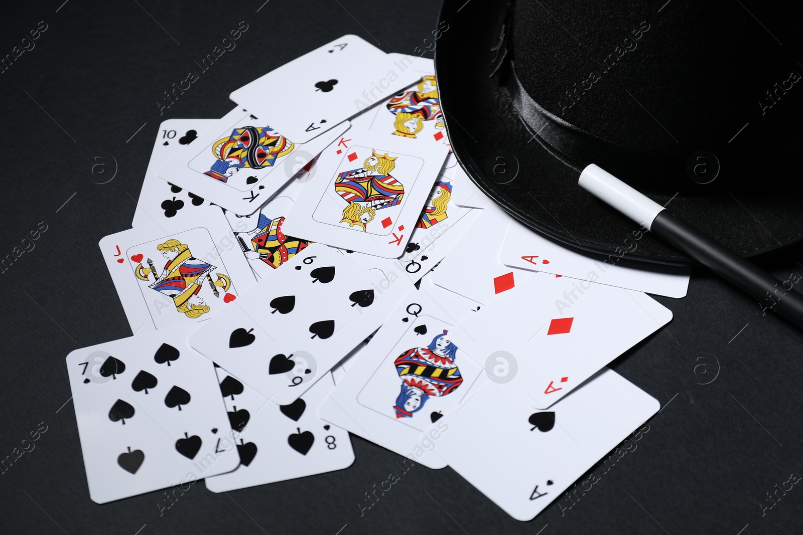 Photo of Playing cards, hat and magic wand on black background, closeup