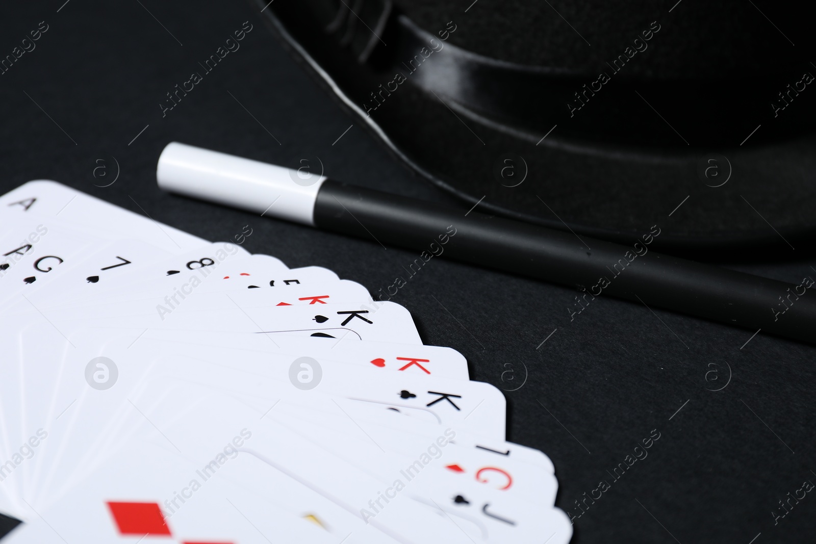 Photo of Playing cards, hat and magic wand on black background, closeup