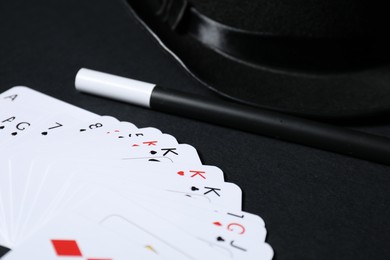 Photo of Playing cards, hat and magic wand on black background, closeup