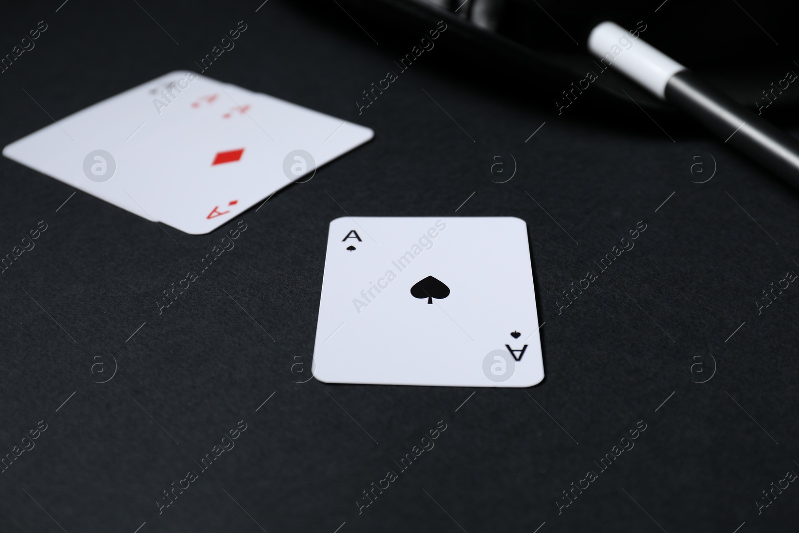 Photo of Playing cards, hat and magic wand on black background, closeup