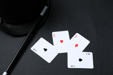 Photo of Playing cards, hat and magic wand on black background, closeup