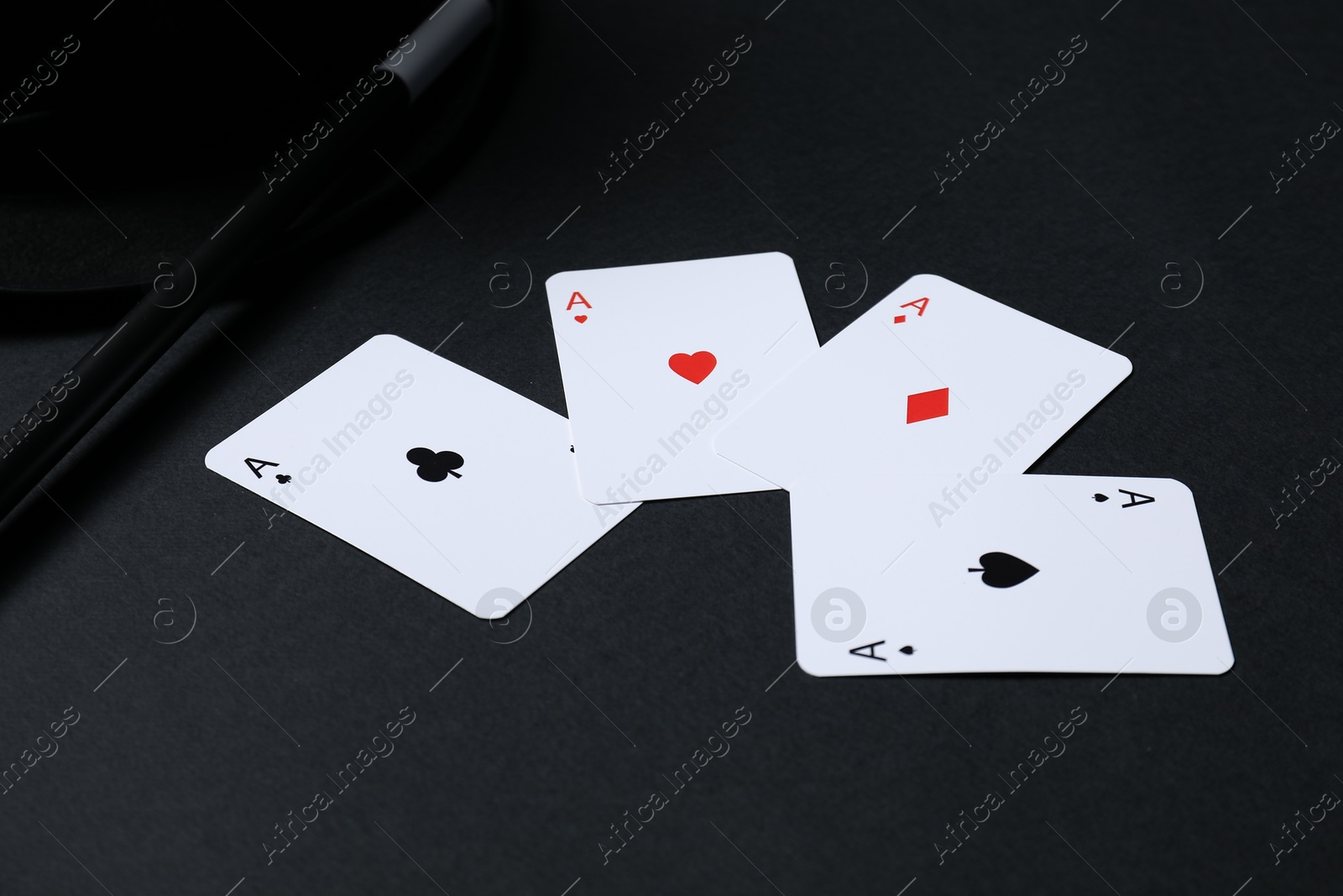 Photo of Playing cards, hat and magic wand on black background, closeup