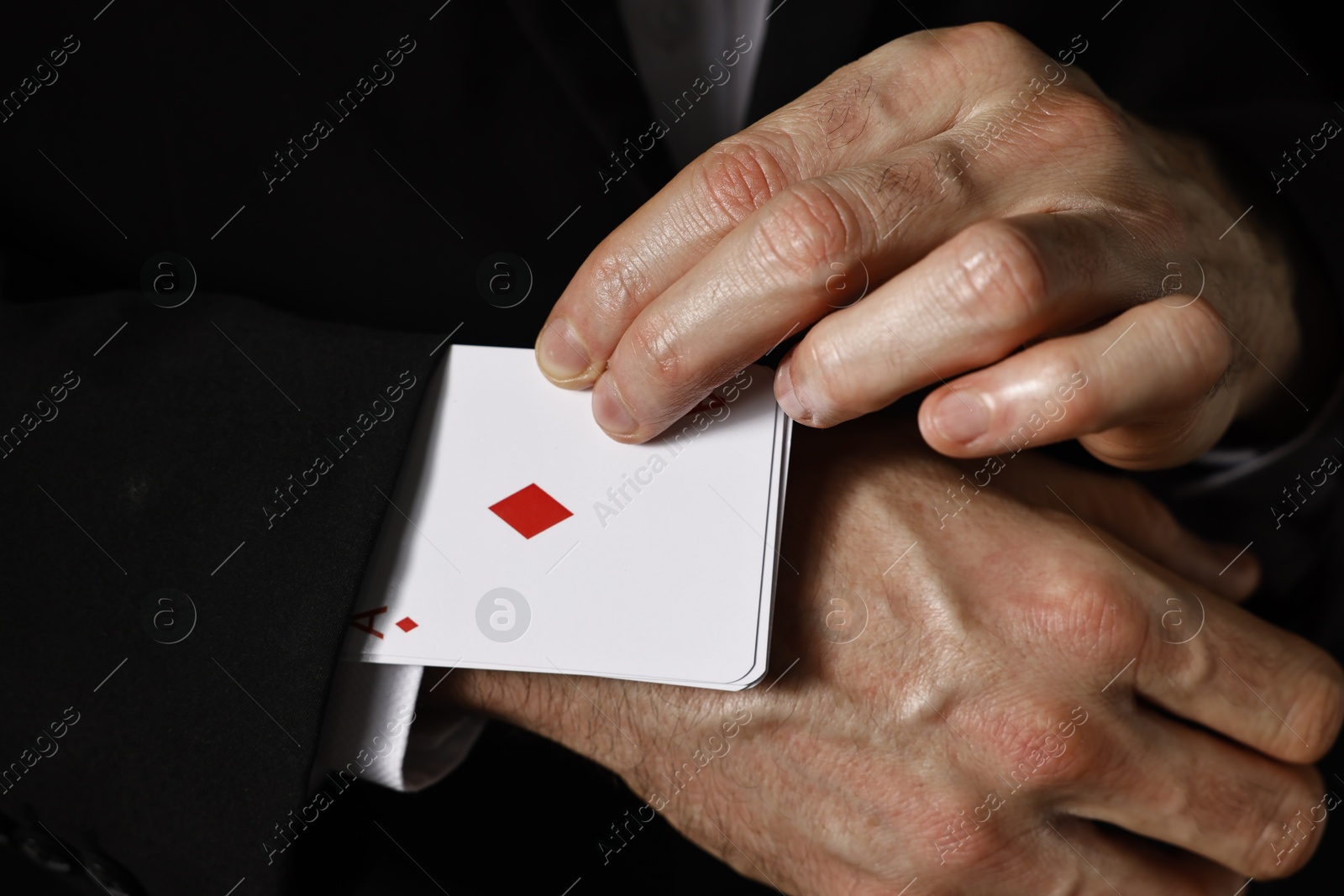 Photo of Illusionist taking playing cards out of sleeve on black background, closeup