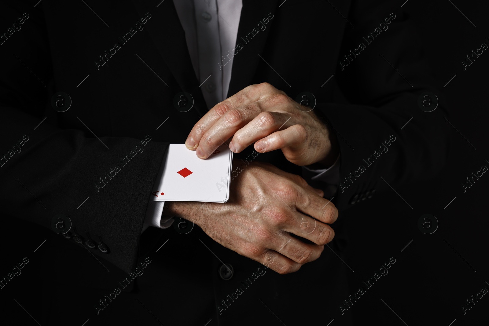 Photo of Illusionist taking playing cards out of sleeve on black background, closeup