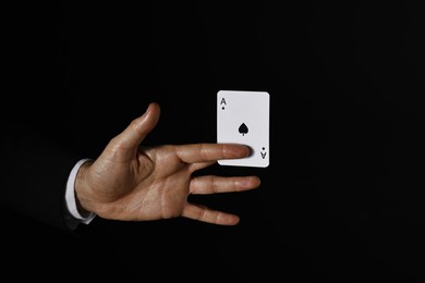 Photo of Illusionist with playing card on black background, closeup