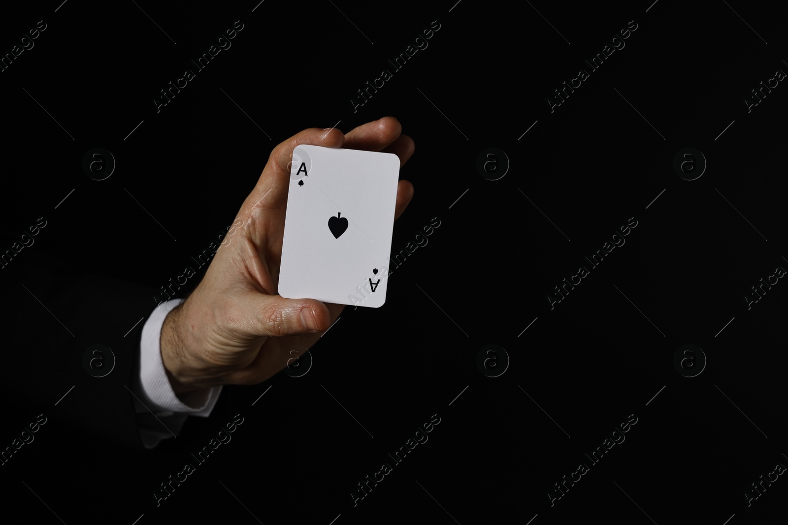 Photo of Illusionist with playing card on black background, closeup. Space for text