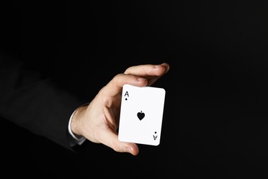 Photo of Illusionist with playing card on black background, closeup