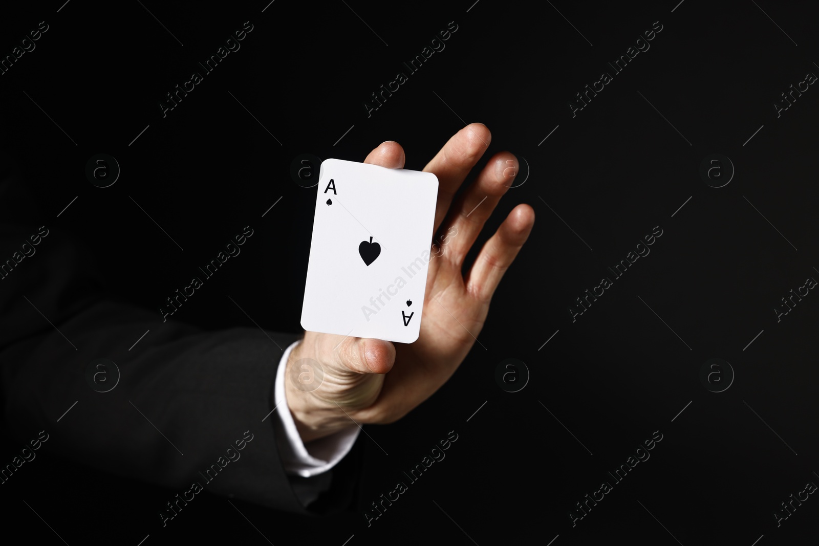 Photo of Illusionist with playing card on black background, closeup