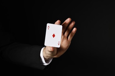 Photo of Illusionist with playing card on black background, closeup