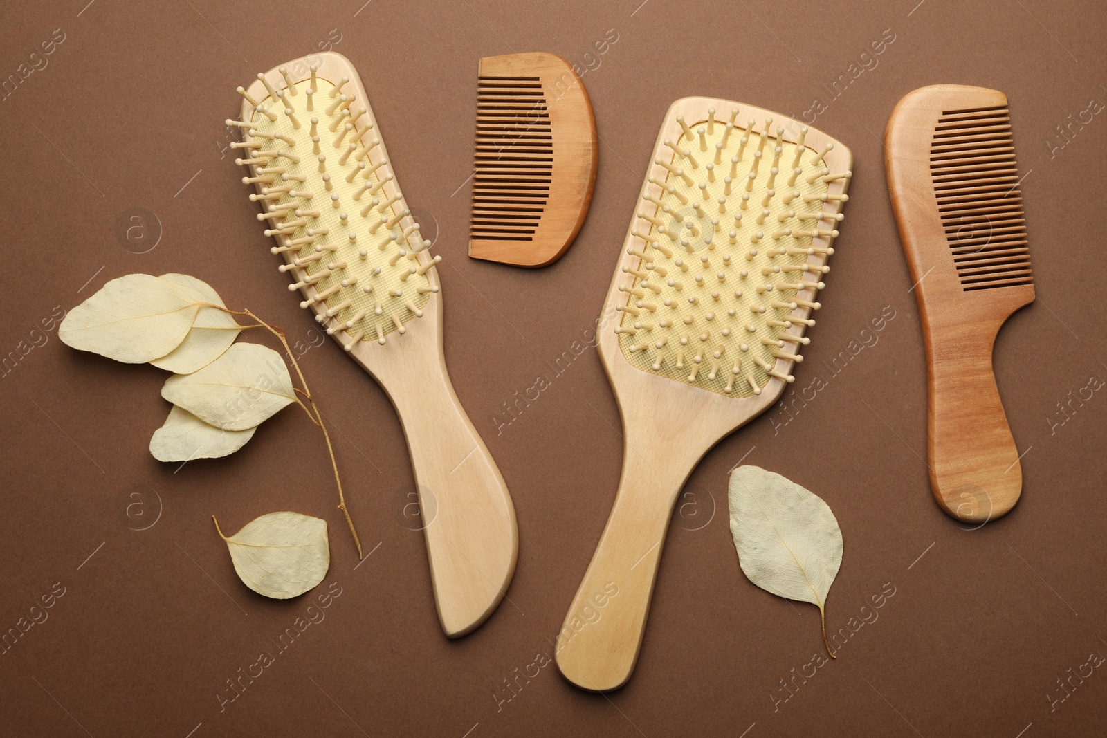 Photo of Wooden hair brushes, combs and leaves on brown background, flat lay