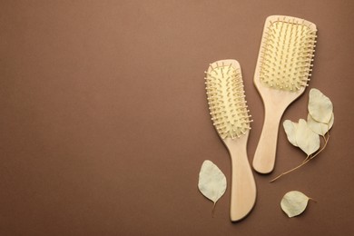 Photo of Wooden hair brushes and plant on brown background, flat lay. Space for text