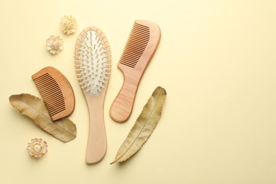 Photo of Wooden hair brush, combs, flowers and leaves on beige background, flat lay. Space for text