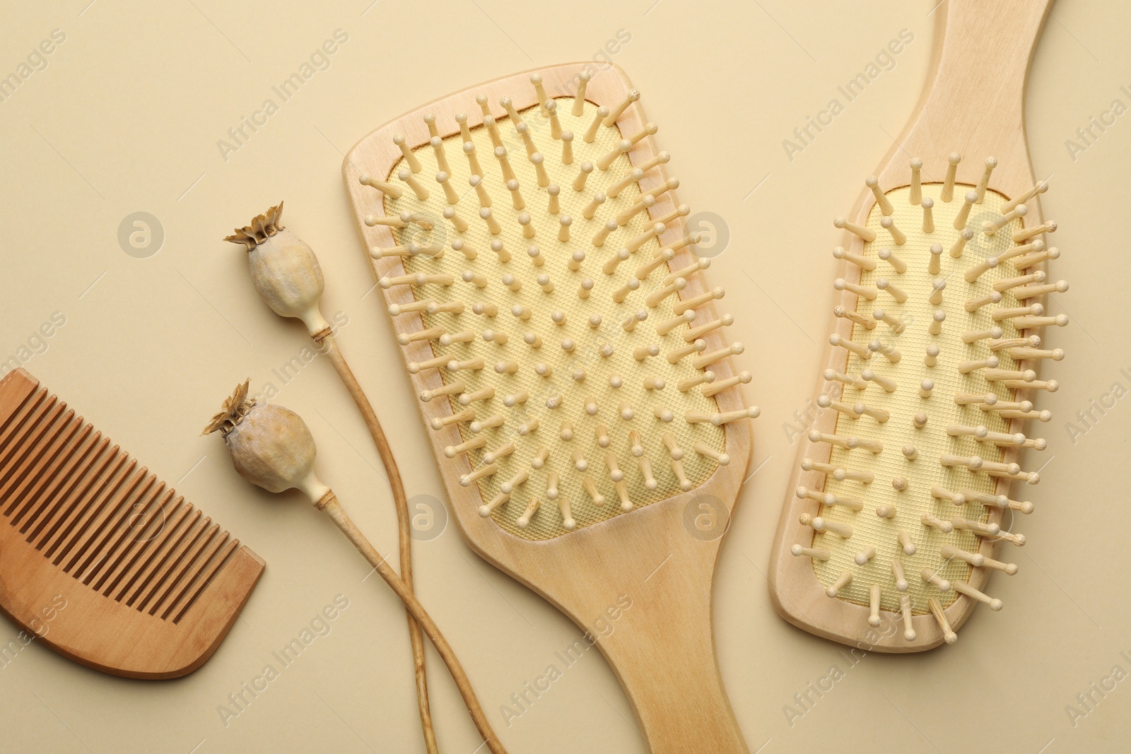 Photo of Wooden hair brushes, comb and poppy heads on beige background, flat lay