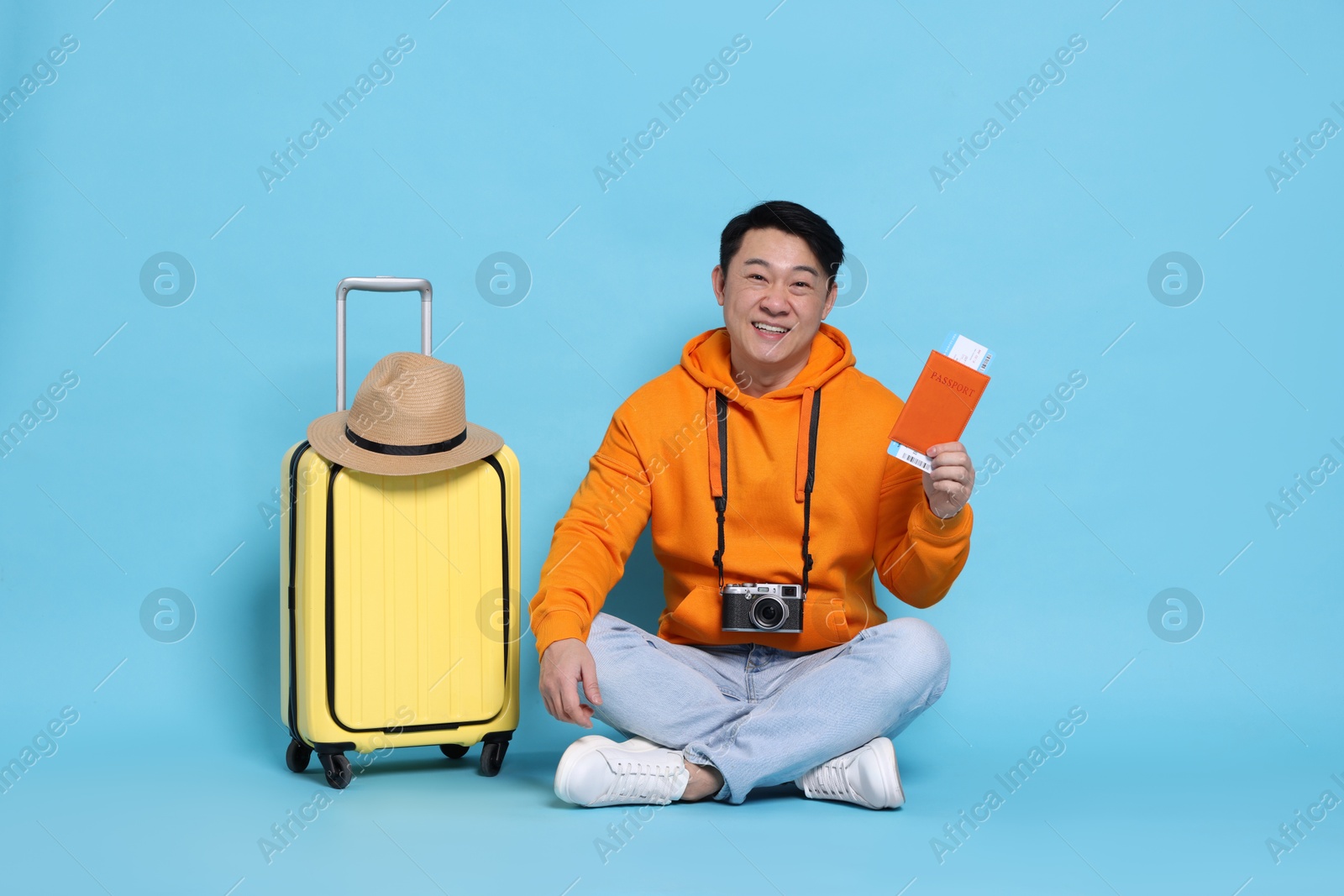 Photo of Traveller with passport, camera and suitcase on light blue background