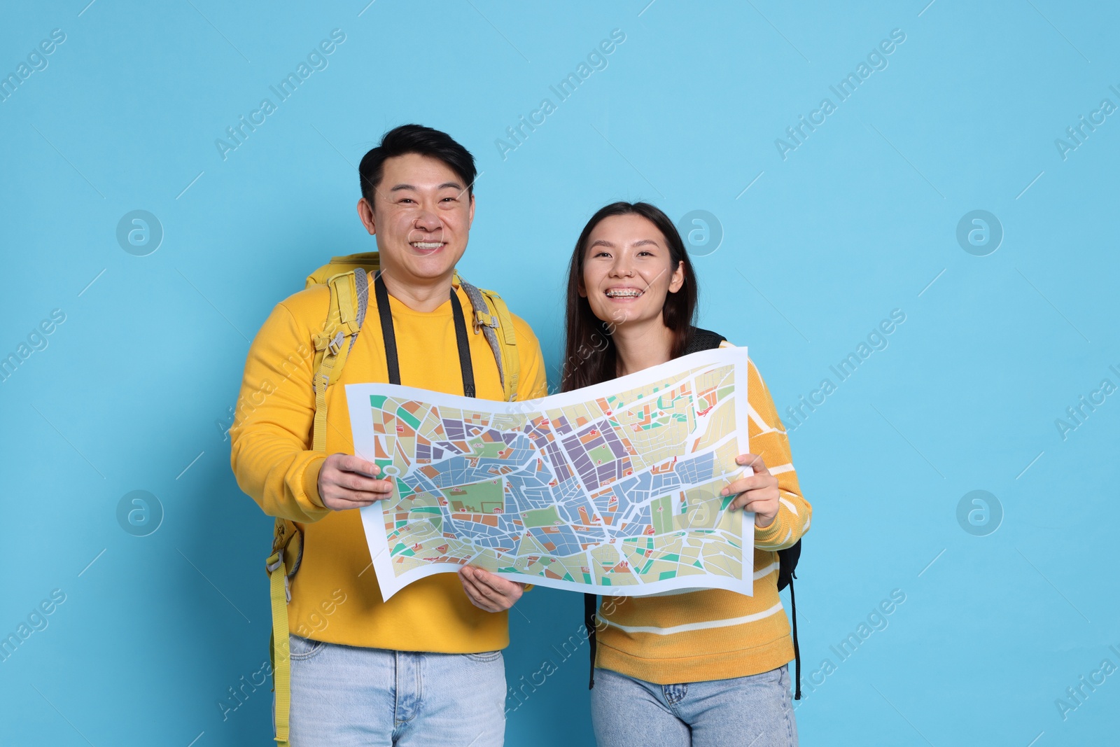 Photo of Happy travellers with map on light blue background