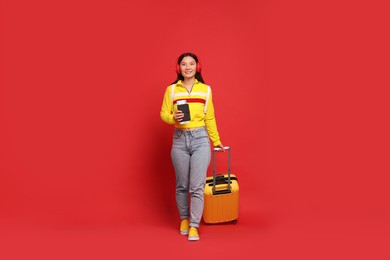 Photo of Happy traveller with passport and suitcase on red background