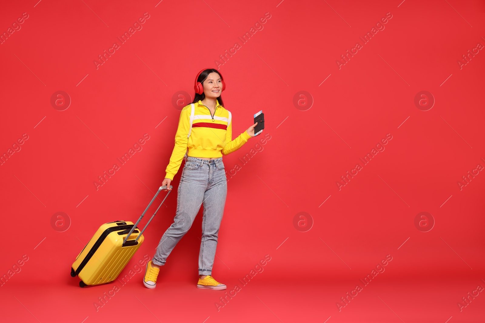 Photo of Happy traveller with passport and suitcase on red background. Space for text