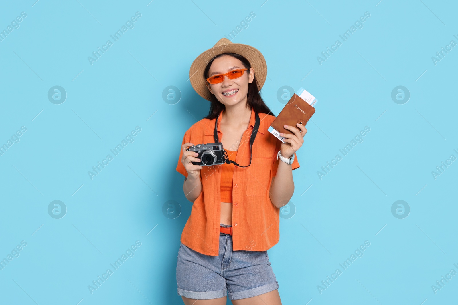 Photo of Happy traveller with passport and camera on light blue background