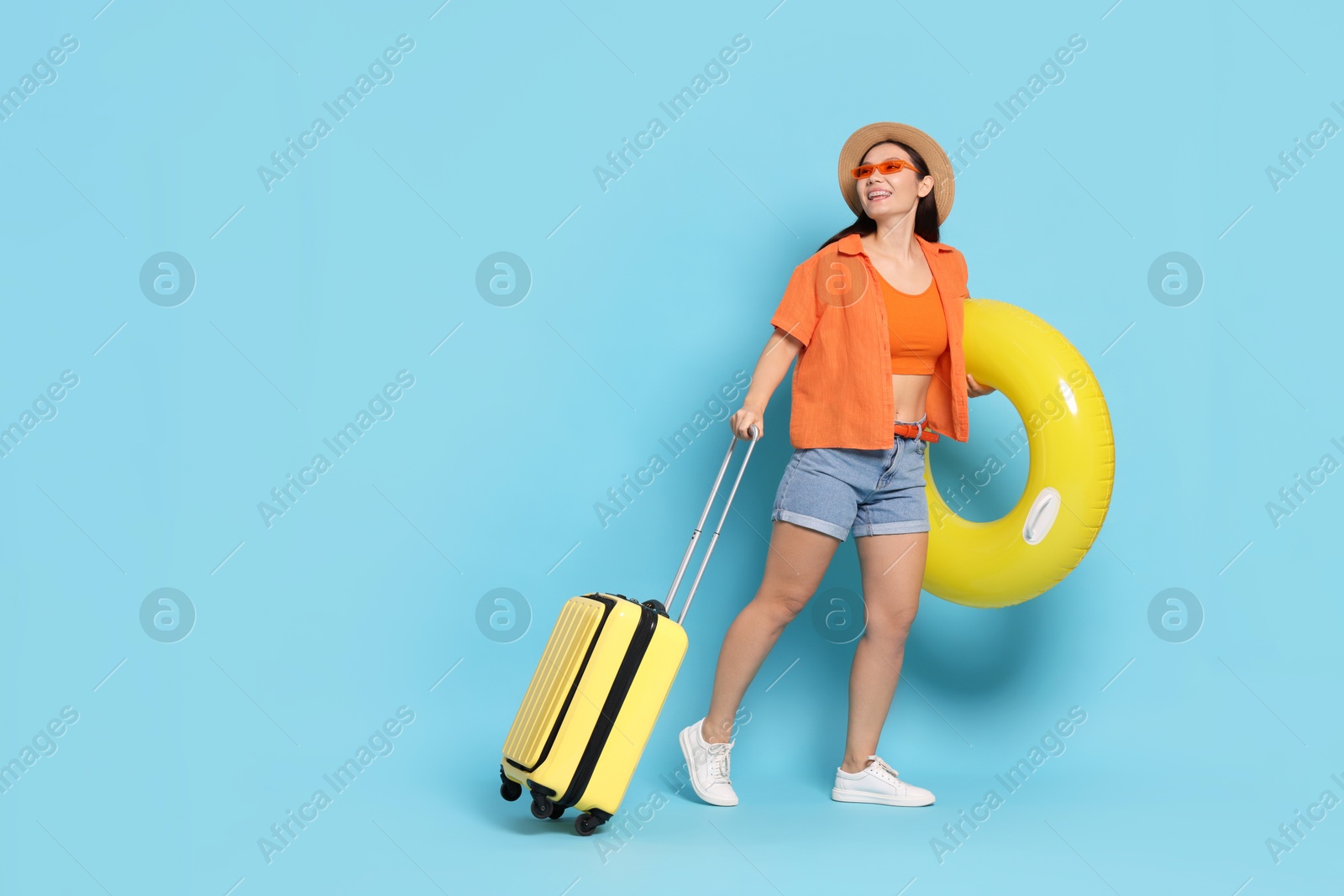 Photo of Happy traveller with inflatable ring and suitcase on light blue background. Space for text