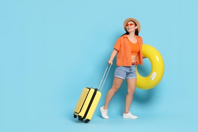 Photo of Happy traveller with inflatable ring and suitcase on light blue background. Space for text