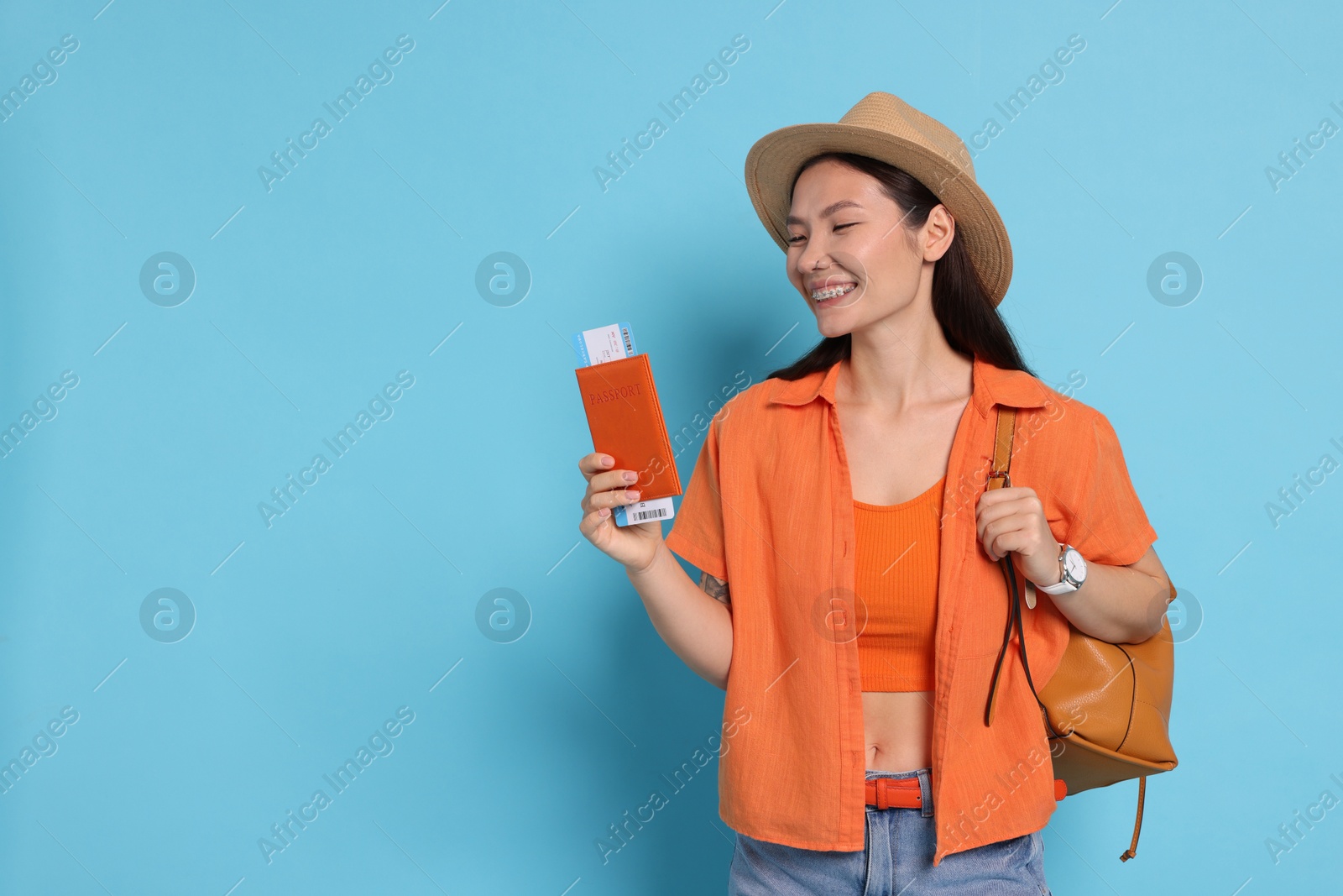 Photo of Happy traveller with backpack and passport on light blue background. Space for text