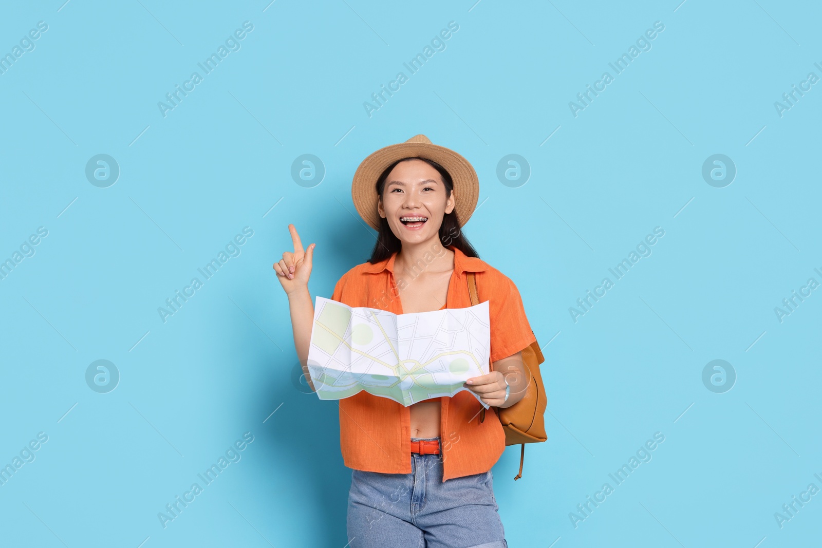 Photo of Happy traveller with backpack and map on light blue background