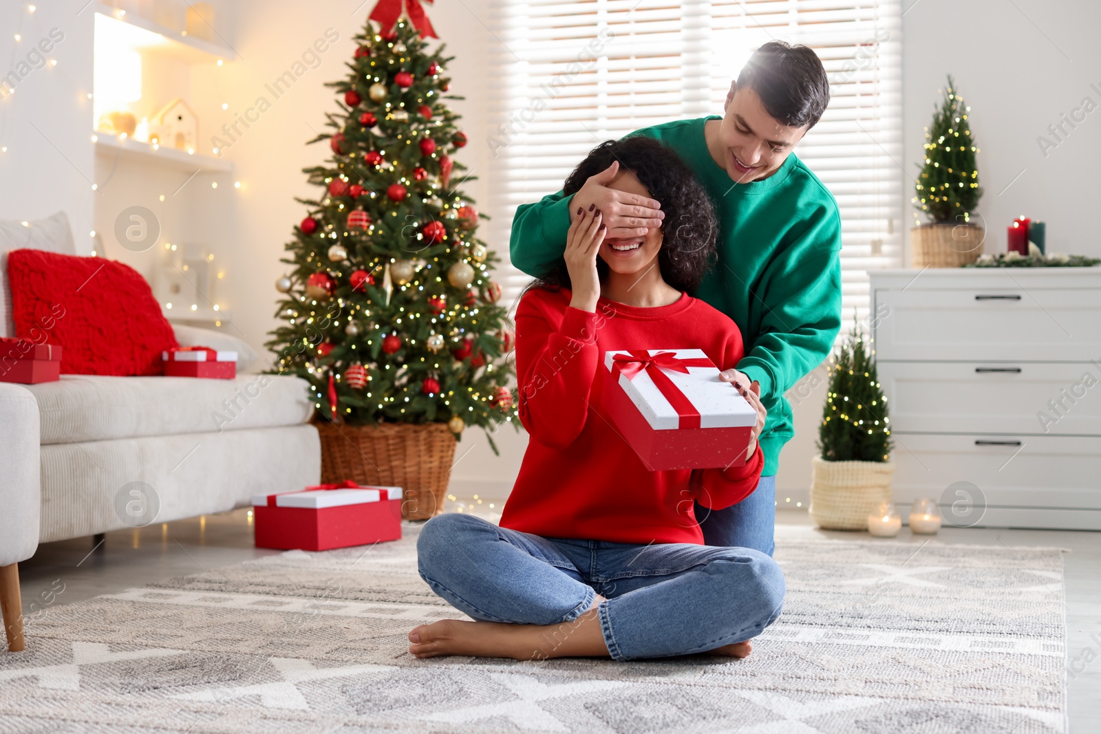 Photo of Happy man surprising girlfriend with Christmas gift at home